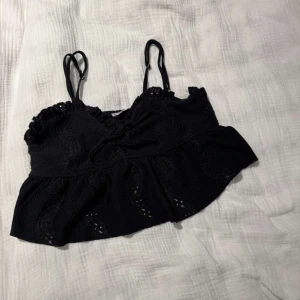 Svart croppad linnetopp - Supersöt svart croppad linnetopp från FB Sister i storlek XS. Toppen har smala justerbara axelband, volangkant nertill och snygga broderade detaljer. Perfekt för varma dagar eller när du vill ha en chill och trendig look 🥰