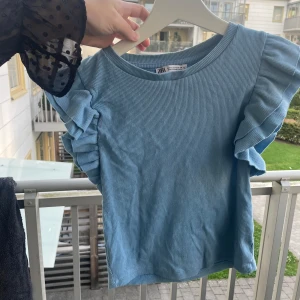 Blå ribbad topp med volangärm Zara - Supersöt ljusblå ribbad topp från Zara med korta volangärmar som ger en extra touch. Toppen har rund halsringning och är i mjuk bomull, perfekt för dig som gillar en chill men ändå trendig stil. Strl s. Använt skick. Går att pruta 