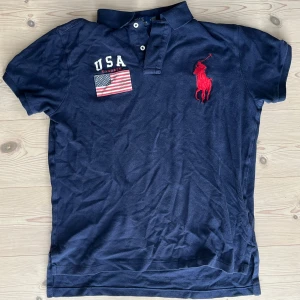 Marinblå Chief keef polo från Ralph Lauren - Snygg marinblå t-shirt från Polo Ralph Lauren med klassisk krage och knappar. Stor röd broderad logga på bröstet och USA-flagga. Nypris 2100. Pris kan diskuteras vid snabb affär.
