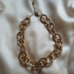 Chunky guldhalsband med tvinnade länkar - Stilrent chunky halsband i guld med stora, tvinnade länkar som ger en cool statement-look. Justerbar längd med kedja och karbinlås. Använd 1 gång, inte tung på. Inköpt för 149kr. Reglerbar längd, 41–49 cm. Zinken i halsbandet är återvunnen.