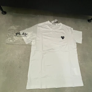 Vit Comme des Garçons Play t-shirt - Helt ny Snygg vit t-shirt från Comme des Garçons Play med det ikoniska svarta hjärtat med ögon broderat på bröstet. Klassisk rund hals och korta ärmar. Tillverkad i mjuk bomull för en clean och stilren look.