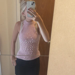 Rosa pärlprydd stickad topp från Zara - Supersöt ljusrosa stickad topp från Zara med hög hals och ärmlös design. Toppen är dekorerad med pärlor framtill för en extra stylish touch. Mjuk och fluffig känsla, perfekt att styla med kjol eller jeans för en trendig look.