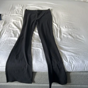 Svarta bootcut byxor med utsvängda ben - Säljer ett par svarta bootcut byxor med riktigt utsvängda ben. De har en clean look utan synliga fickor eller detaljer och är perfekta om du gillar en stilren vibe. Sitter snyggt i midjan och är gjorda i ett mjukt material som känns skönt hela dagen.