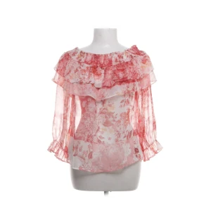 Blommig offshoulder blus från Zara - Superfin blommig blus från Zara i tunnt, transparent tyg. Offshoulder-modell med volangdetaljer och trekvartsärmar. Färgerna går i rosa, rött och vitt och blusen har en luftig och romantisk vibe. 