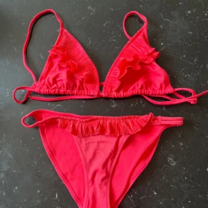 Bikini med volangdetaljer - Superfin rosaröd bikini med volangdetaljer på både överdel och underdel. Triangelformad topp med smala axelband och knyt i ryggen. Bikinitrosan har låg midja och matchande volang längs linningen. Priset kan diskuteras❣️❣️