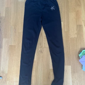 Konståknings byxor - Svarta leggings från K-Skate i stretchigt material. De har en snygg strassdetalj på höften som ger lite extra bling. Perfekta för dig som gillar att sticka ut på träningen eller i vardagen. Mjuka och bekväma med elastisk midja.