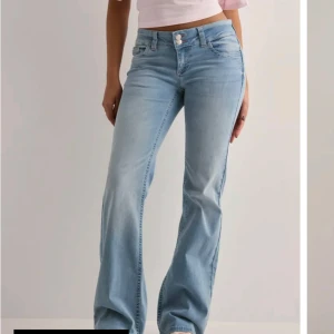 Ljusblå bootcut jeans med brodyr - Snygga ljusblå jeans med bootcut passform och låg midja. Jeansen har coola bakfickor med rosa broderad zigzag-detalj. Klassisk femficksmodell i mjukt denimtyg, perfekta för en avslappnad och trendig look.