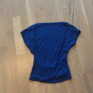 Blå topp med öppen rygg - En cool blå topp med fin passform. T-shirten har en enkel design utan mönster och är tillverkad i ett mjukt, tunt material som känns skönt mot huden. Perfekt för dig som gillar en avslappnad stil. Den är öppen vid ryggen som syns på bild 2💗