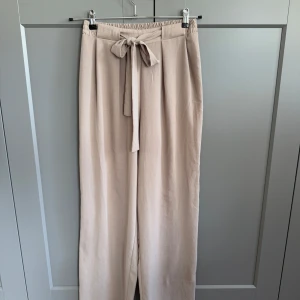 Beiga vida byxor med knyt från Zara - Säljer ett par beiga byxor från Zara i storlek M. De har hög midja med resår och ett snyggt knytband framtill. Vida ben och mjukt, lätt material som känns riktigt skönt. 