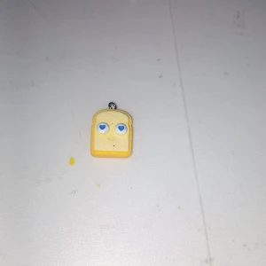 Gult toast-halsband i syntet - Roligt halsband med en berlock formad som en gul toastskiva. Perfekt för dig som gillar unika och lekfulla accessoarer. Hängs i en liten metallögla och är tillverkad i syntetmaterial.