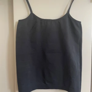 Svart linnetopp från ONLY - Enkel och stilren svart linnetopp från ONLY med smala axelband. Toppen är i stretchigt material med 94% Tactel och 6% Lycra, vilket gör den mjuk och följsam. Perfekt att styla med jeans eller kjol för en clean look. Liten som S