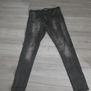Svarta skinny jeans från ICON2 - Snygga svarta skinny jeans från ICON2 med slitningar och hål på benen för en cool, sliten look. Jeansen har fem fickor, dragkedja och knapp framtill samt tydliga tvättade detaljer. Perfekta för dig som gillar streetstyle. Storlek w31 l 32