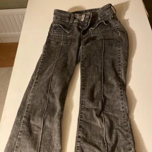 Grå bootcut jeans från Nelly - Snygga grå jeans från Nelly med bootcut passform och slitna detaljer på benen. Jeansen har mellan midja, dubbla knappar i linningen och coola fickor framtill. Är öppen för bud!!