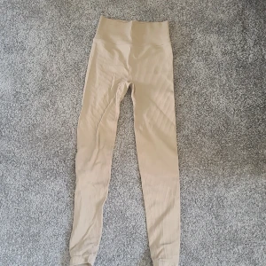Beige ribbade leggings NA 146/152 - Snygga beige leggings från NA i storlek 146/152. De är ribbade och har hög midja för extra komfort. Perfekta för chill eller träning, med stretchigt material som sitter tajt och följer kroppen.