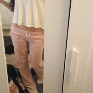 Ljusrosa lågmidjade juicy byxor  - Säljer ett par ljusrosa mjukisbyxor med låg midja och snörning framtill. Byxorna har raka ben och stora fickor framtill. Perfekta för chill dagar eller när du vill vara extra bekväm. Mjukt material som känns skönt mot huden.