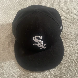 Svart White Sox keps från New Era - Säljer en svart keps från New Era med broderad vit White Sox-logga framtill. Klassisk modell med rak skärm och snygg passform. Perfekt för dig som gillar sportiga och stilrena accessoarer.