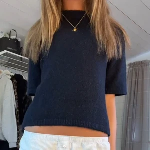 Mörkblå stickad kortärmad tröja - En enkel och stilren mörkblå stickad tröja med korta ärmar och rak passform. Tröjan har en klassisk rund halsringning och är perfekt att matcha med både jeans och kjol för en clean look.