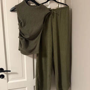 Olivgröna ribbade byxor med snörning - Snygga olivgröna byxor med ribbad struktur och avslappnad passform. Byxorna har resår och snörning i midjan för extra komfort. Perfekta för en chill och trendig look.