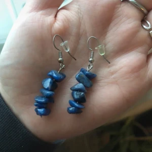 Blå örhängen med sodalitstenar - Unika örhängen med blå oregelbundna sodalitstenar på silverfärgade krokar. Ena örhänget har flera små stenar staplade på rad, medan det andra har en ensam blå sten. Handgjorda.