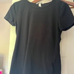 Svart t-shirt från H&M, storlek S - En basic svart t-shirt från H&M i storlek S. T-shirten har rund halsringning och korta ärmar, perfekt att matcha med jeans eller kjol. Tillverkad i mjuk bomull för en skön känsla hela dagen. Kan diskutera priset