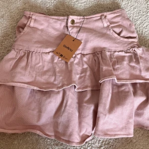 Rosa volangkjol i jeansliknande material  - Supersöt ljusrosa kortkjol i manchester med volanger och klassiska fickor fram. Kjolen är gjord i ett skönt stretchigt material och har en lågmidjad modell. Perfekt för dig som gillar en feminin och trendig look. Stretchig, passar därför flera storlekar. Lappen kvar från Sellpy