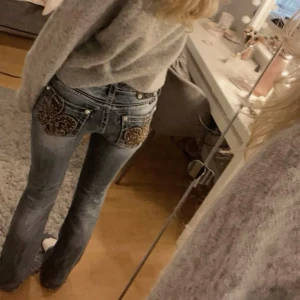 Miss Me ljusblå bootcut jeans med brodyr - Säljer ett par ljusblå jeans från Miss Me med snygg broderad design och nitar på bakfickorna. Jeansen har bootcut passform, låg midja och klassisk femficksmodell. Materialet är mjukt denim i bomull med lite stretch för extra komfort.