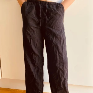 Svarta linnebyxor från Gina Tricot - Svarta linnebyxor från Gina Tricot med avslappnad passform och resår i midjan. Byxorna har snörning framtill och raka ben, perfekta för en chill och stilren look. Materialet är svalt och skönt, och de har fickor på sidorna.