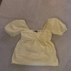 Gul blus med puffärmar - Söt ljusgul blus med puffiga korta ärmar och rynkade detaljer över bysten. Blusen har en luftig passform och fyrkantig ringning, perfekt för en somrig look.
