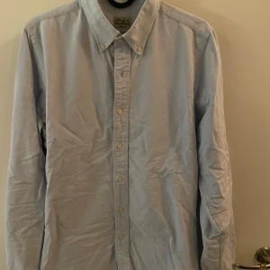 Ljusblå skjorta Made in the Shade  - Snygg ljusblå skjorta från Made in the Shade i slim fit-modell. Skjortan har klassisk krage, knäppning framtill och långa ärmar. Perfekt för dig som gillar en stilren och enkel look.