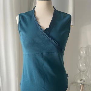 Blå omlottopp från Street One - Snygg blå omlottopp från Street One med ärmlös design och v-ringning. Toppen har volangkant längs ringningen och är gjord i mjuk bomull. Perfekt för dig som gillar stilrena och bekväma plagg med en twist.