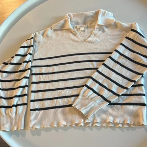 Randig stickad tröja från Gina Tricot - Snygg stickad tröja från Gina Tricot i vitt med mörkblå  horisontella ränder. Tröjan har en bred krage, v-ringning och långa ärmar med ribbade muddar. Perfekt för dig som gillar en klassisk men trendig look. Från Gina Tricot