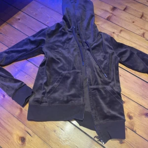 Brun velour hoodie Juicy Couture XS -  brun hoodie från Juicy Couture i mjuk velour med broderad JC-logga på bröstet, huva med snörning, dragkedja framtill och två fickor. Använd att par fåtal gånger.