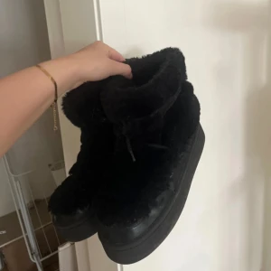 Svarta fluffiga boots med platåsula - Mysiga svarta boots med fluffigt pälsfoder och platåsula. Skorna har snörning framtill och detaljer i skinn, vilket ger en cool och chunky look. Perfekta för kalla dagar när du vill hålla stilen och värmen. Bra skick förutom att de är lite nedtrampade på högra skon men inget som syns eller påverkar funktionen. I övrigt väldigt sköna och bekväma. 