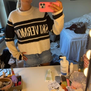 Randig stickad tröja SKIVERMONT - Säljer en stickad tröja i vitt och svart med breda ränder och texten SKIVERMONT framtill. Tröjan har en avslappnad passform, rund halsringning och långa ärmar. Perfekt för dig som gillar en sportig och trendig look.