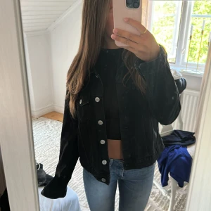 Svart jeansjacka med silvriga knappar - Säljer en svart jeansjacka med klassisk krage och silvriga knappar framtill. Jackan har två bröstfickor med lock och knapp, samt en rak passform som ger en chill vibe. Perfekt att slänga över en hoodie eller crop top.