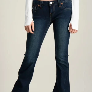 True Religion Joey Low Rise Flare Jeans - Snygga mörkblå jeans från True Religion, modell Joey Low Rise Flare. De har låg midja, utsvängda ben och coola bakfickor med dekorativa sömmar och knappar. Extremt bra skick, aldrig använda.