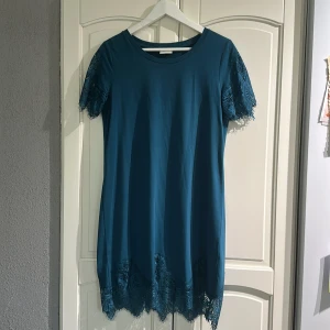 Blå kortklänning med spets från Vila - Supersnygg blå kortklänning från Vila med spetsdetaljer på ärmar och nederkant. Klänningen har rund halsringning och korta ärmar med vacker spets som ger en extra touch. Perfekt för dig som vill ha en enkel men ändå unik look. Använd ett fåtal ggr