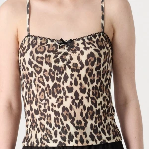 Gina Tricot Leopardmönstrad linnetopp med rosett - Säljer en leopardmönstrad linnetopp med tunna axelband och liten svart rosett framtill. Toppen har svarta spetsdetaljer längs överkanten och är figurnära i modellen. Perfekt för dig som vill sticka ut med ett djurmönster. Helt oanvänd.