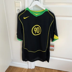 Nike Total 90 svart L - Nike Total 90 remake i svart med gula detaljer och gröna inslag. Tröjan har korta ärmar, meshpaneler för extra ventilation och en stor gul 90-logga på bröstet. En oversize känsla. Tillverkad i lätt och ventilerande polyester.  Nypris: 750