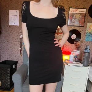 Svart klänning med spets - Svart klänning med blommönstrad spetsdetalj på ärmarna. Lite goth känsla om man skulle stylea den så men funkar även som en vanlig, simpel klänning :) Väldigt bekväm!