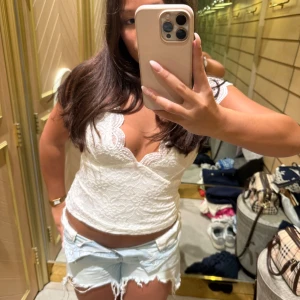 Vit spetsig omlottopp med öppen rygg - Supersöt vit topp i spets med omlott framtill och djup v-ringning. Toppen är croppad, har små ärmar och en öppen rygg med fina spetsdetaljer. Perfekt för sommarens varma dagar och ger en romantisk vibe.