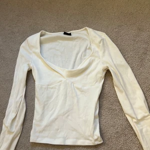 Vit långärmad topp Gina Tricot - Snygg vit långärmad topp från Gina Tricot i storlek XXS. Toppen har en djup v-ringning och figurnära passform. Tillverkad i mjuk bomullsmix som känns skön mot huden. Perfekt att styla med jeans eller kjol för en clean look. Jättefin.