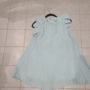 Ljusblå plisserad klänning med volangärm - Superfin ljusblå/ljusgrön klänning med plisserat tyg och volangärmar. Klänningen har rund halsringning och en liten knapp i nacken. Luftig och flowy modell som ger en riktigt söt och somrig vibe.