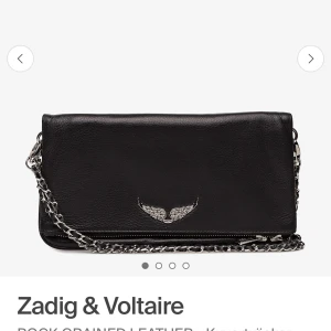 Svart kuvertväska Zadig & Voltaire - Stilren svart kuvertväska i skinn från Zadig & Voltaire med silverfärgad kedjerem och ikonisk vingdetalj framtill. Väskan har dragkedja både bak och upptill, perfekt för att hålla koll på dina grejer. Snygg och edgy accessoar som lyfter varje outfit.