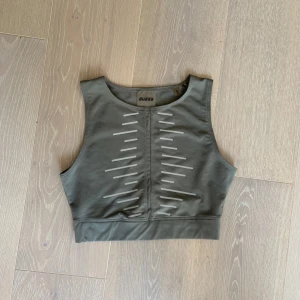 Grön  träningstop från Guess - Snygg grön träningstop från Guess med coola vita detaljer framtill. Toppen är ärmlös och har en sportig vibe, perfekt för träning eller chill dagar. Tillverkad i stretchigt syntetmaterial som sitter skönt på kroppen. Logga på både fram- och baksida.