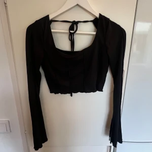 Svart croppad långärmad topp med knyt - Svart croppad topp med långa ärmar och snygg fyrkantig ringning. Toppen har ribbad struktur och knytning i ryggen🤩