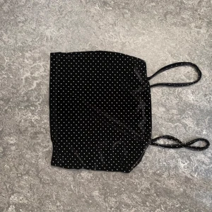 Svart prickig linnetopp från Bik Bok - Säljer en svart linnetopp från Bik Bok med tunna axelband och små vita prickar över hela tyget. Toppen har en glansig finish och är perfekt för att lyfta en outfit med lite extra stil.