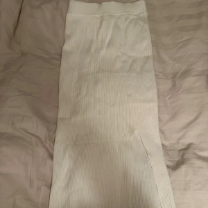 Vit ribbad långkjol - Säljer en vit ribbad långkjol med hög midja och en snygg slits på sidan. Kjolen har en enkel och stilren design som passar perfekt till många olika outfits.