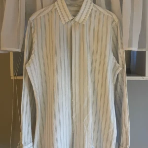 Vit och grönrandig skjorta från Livergy - Klassisk vit skjorta med tunna gröna ränder från Livergy. Skjortan har lång ärm, krage och knäppning framtill.