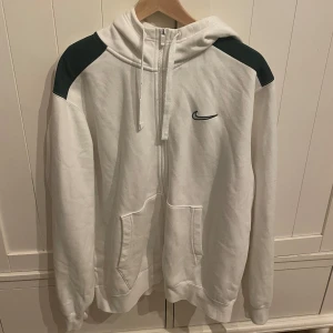 Vit nike hoodie - Vit hoodie med mörk gröna detaljer köpt från JD.  Nypris runt 500-600kr. Använd max två gånger hemma och har inga skador. Alltså nästan helt ny. 